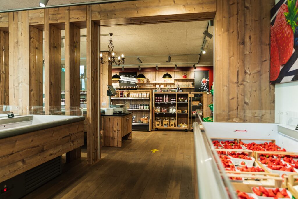 Ein Hofladen von innen mit einer Kühltruhe voller Erdbeeren auf der rechten Seite. Hinten an der Wand stehen Regale mit vielen Produkten.
